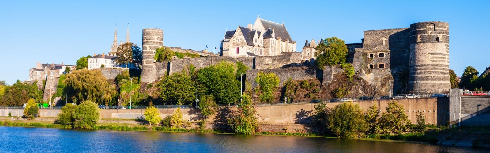 A brown castle with various round turrets sits on the edge of a river. 